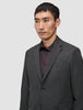 Ein Mann, der einen Motion Blazer Slim in der Farbe Pepper Grey aus 360°-Stretchstoff über einem dunklen Hemd mit Knopfleiste trägt – ein Design, das sich durch eine klare, skandinavische Ästhetik auszeichnet.