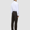 Eine Person, von hinten gesehen, die ein weißes Hemd, eine Motion Suit-Hose in der Passform Regular in der Farbe Cognac und schwarze Anzugschuhe trägt und damit einen eleganten Look präsentiert.