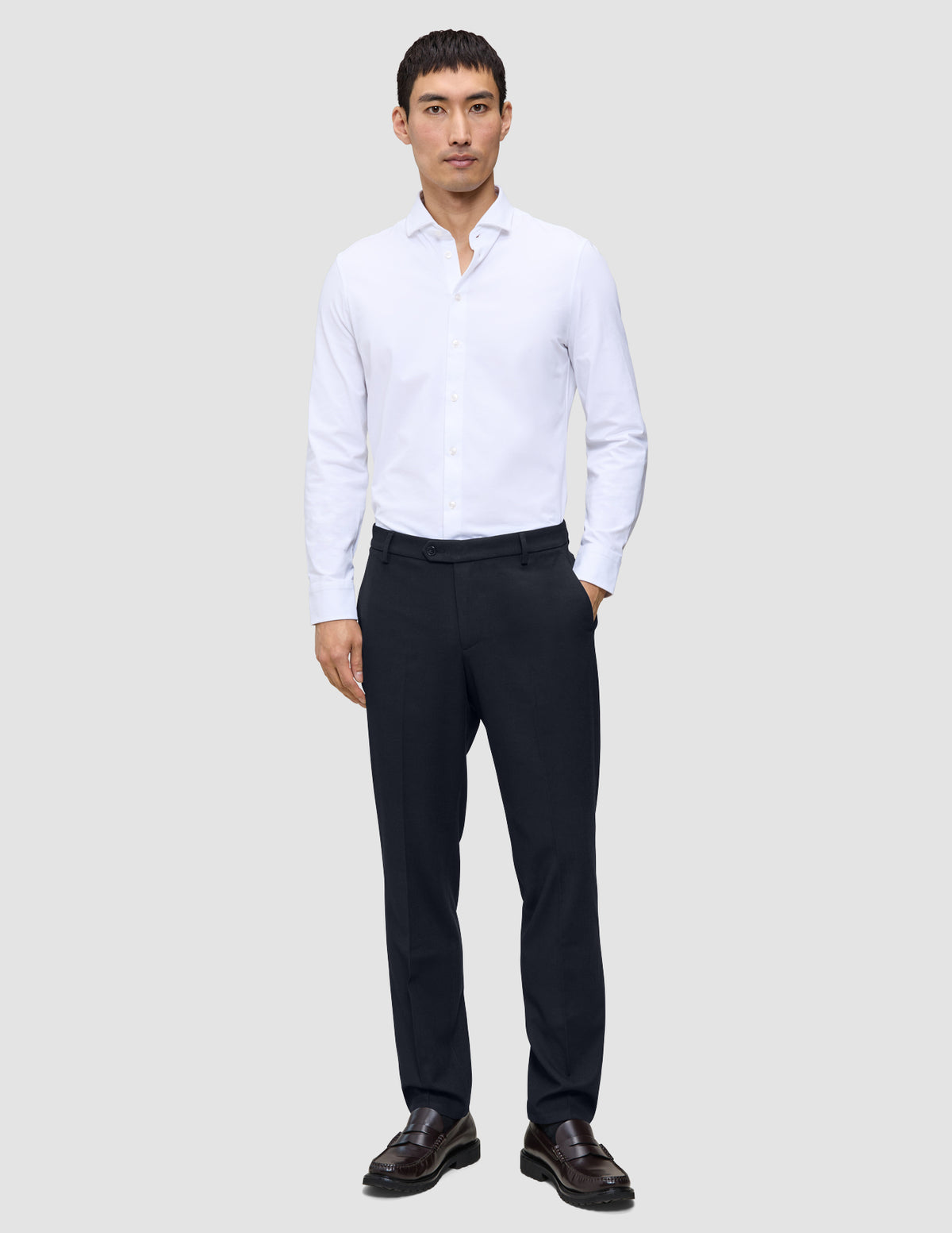 Ein Mann, der ein weißes Hemd, eine Motion Suit-Hose in der Passform Regular in Mitternachtsblau mit 360°-Stretch sowie dunkle Slipper trägt.