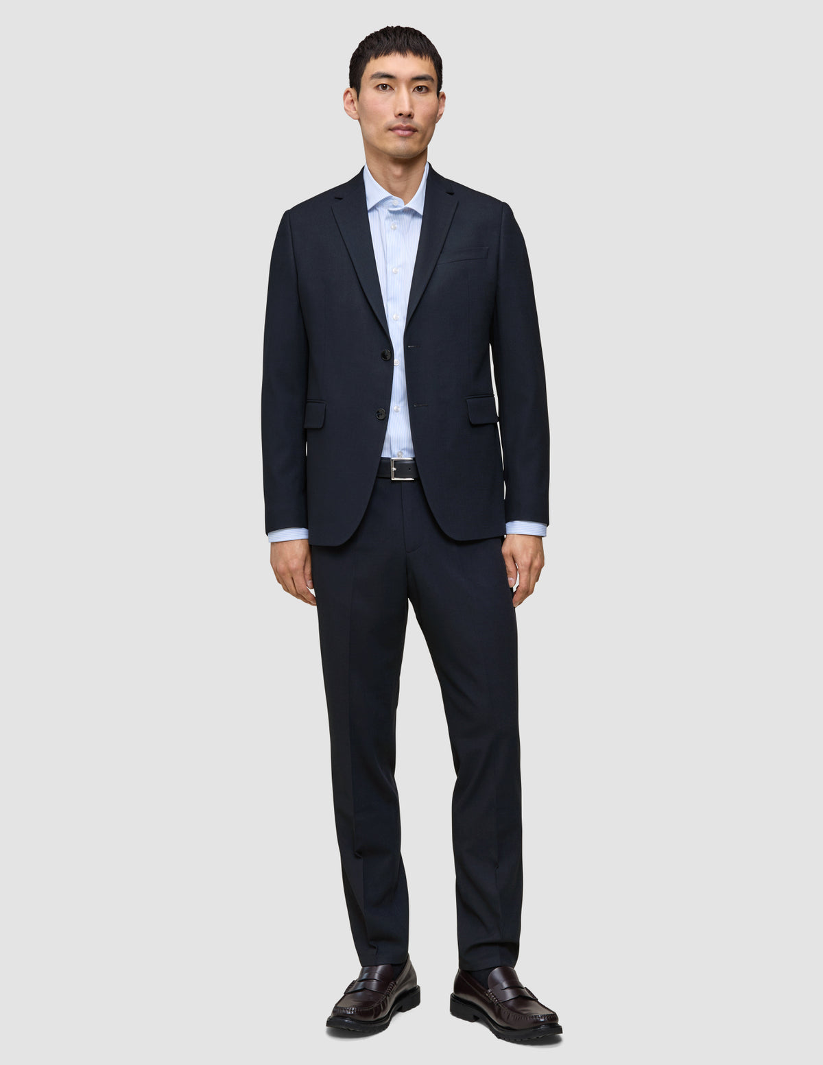 Ein Mann trägt ein atmungsaktives, dunkelblaues Sakko mit 360°-Stretch sowie eine dazu passende Motion Suit-Hose in der Passform Regular in Mitternachtsblau, dazu ein hellblaues Hemd mit Knöpfen und dunkle Slipper.