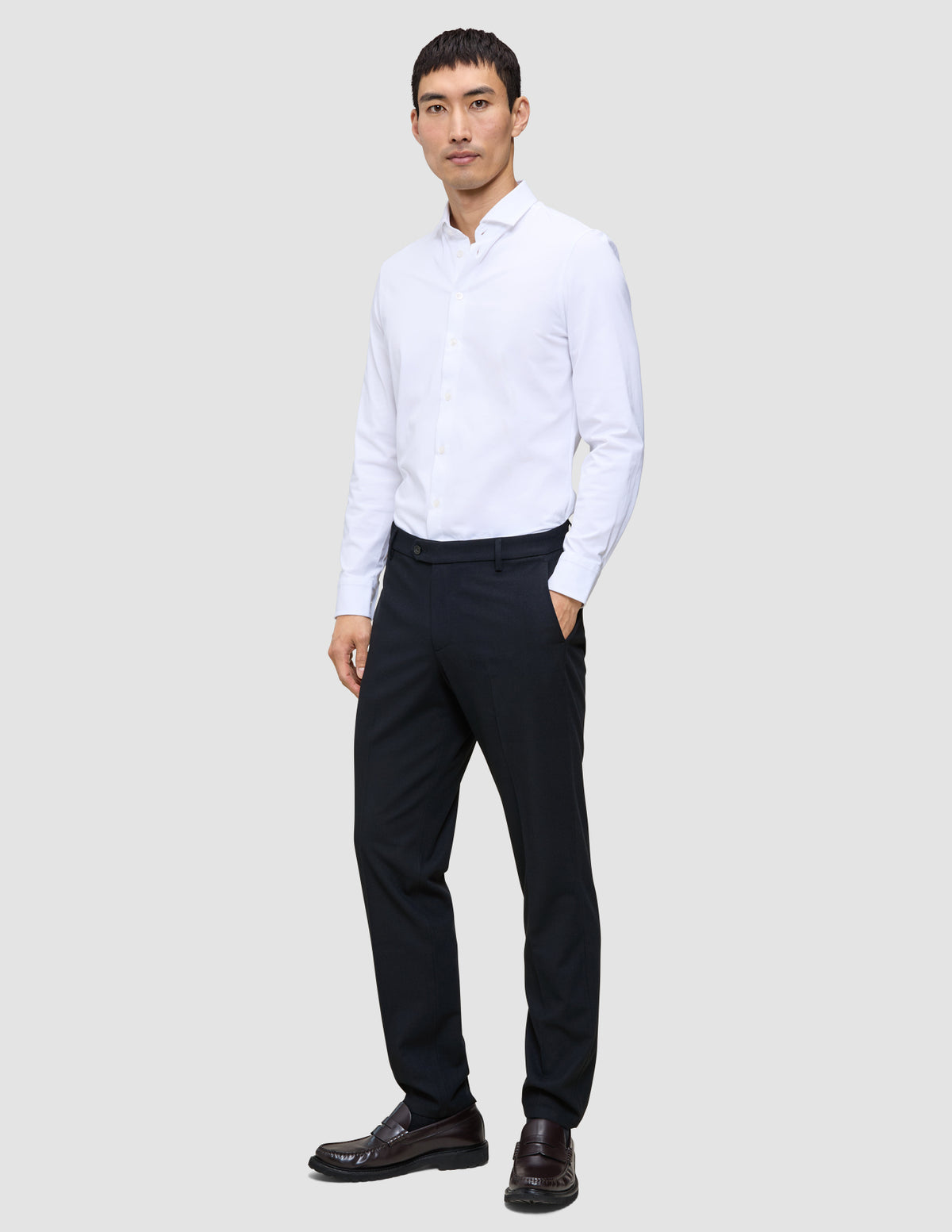 Ein Mann steht mit der Hand in der Tasche da; er trägt ein weißes Hemd und eine Motion Suit-Hose in der Passform Regular in Mitternachtsblau.