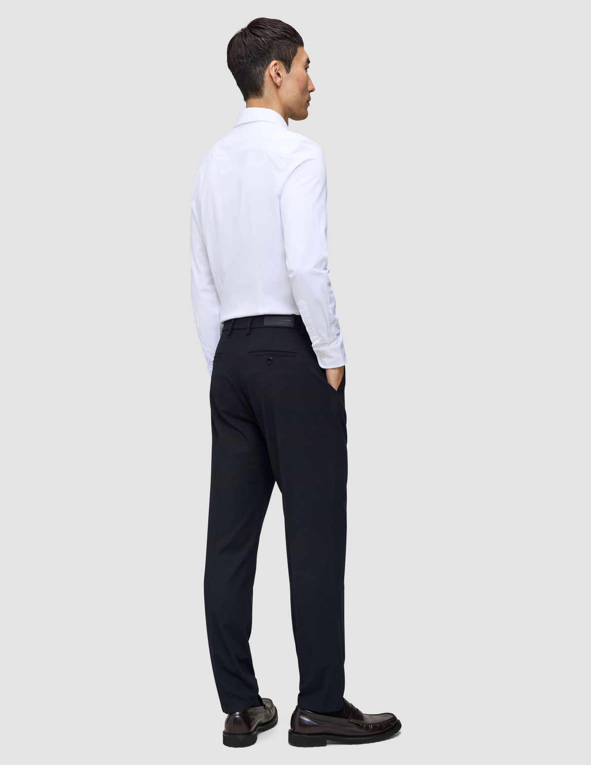 Ein Mann, von hinten gesehen, der ein weißes Hemd, Slipper und eine Motion Suit-Hose in der Passform Regular in Mitternachtsblau trägt.