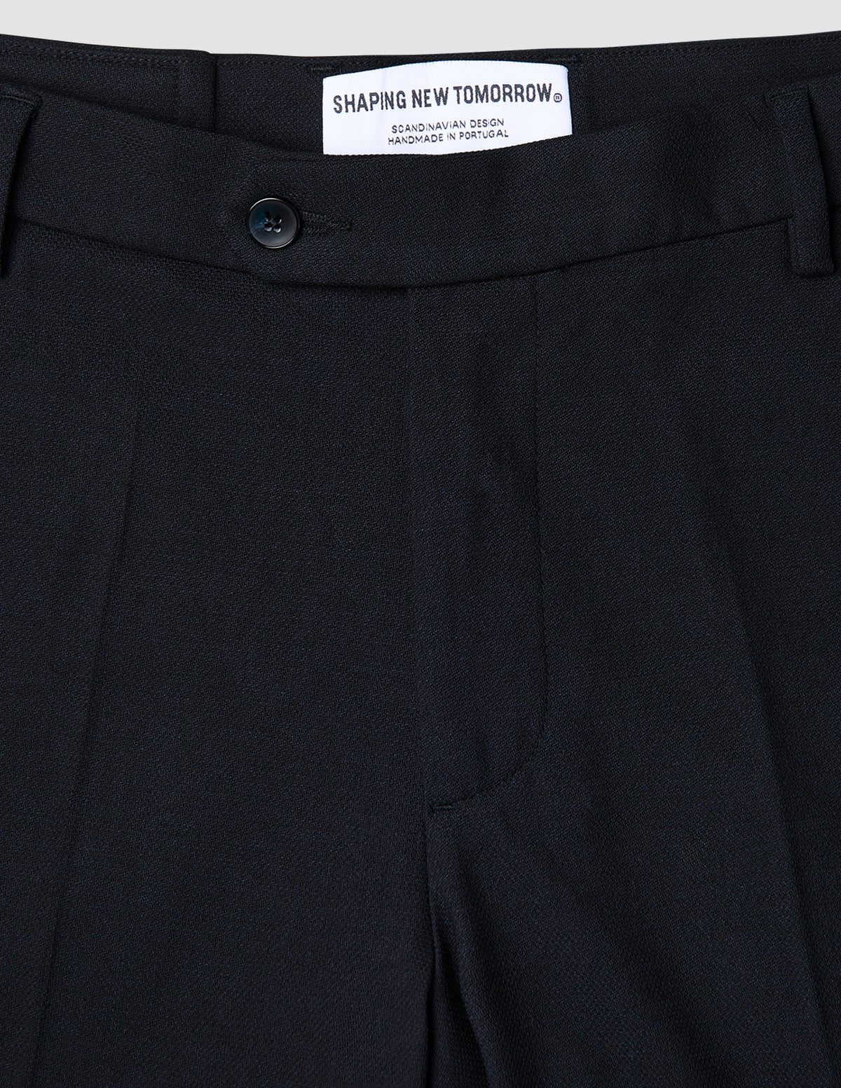 Nahaufnahme einer atmungsaktiven, dunkelblauen Motion Suit-Hose in Regular-Passform in Mitternachtsblau mit 360°-Stretch, Knopfverschluss und einem Innenetikett mit der Aufschrift Shaping New Tomorrow, Scandinavian Design und Handmade in Portugal.