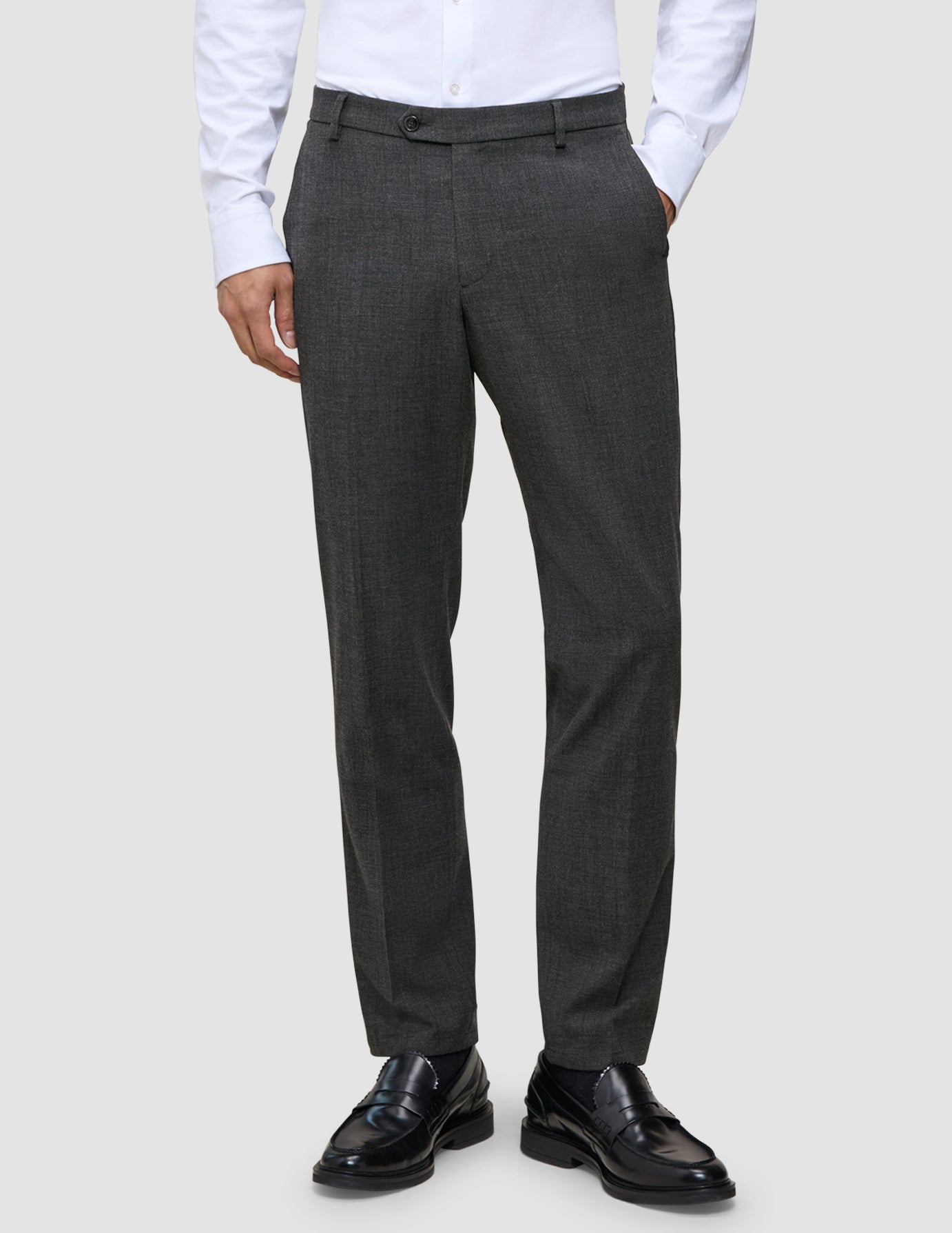 Eine Person, die eine Motion Suit Pants Regular Pepper Grey, ein weißes Hemd und schwarze Slipper trägt.