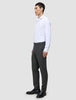Ein Mann in einem weißen Hemd und einer grauen Motion Suit-Hose in der Farbe Regular Pepper Grey steht im Profil und trägt schwarze Slipper.