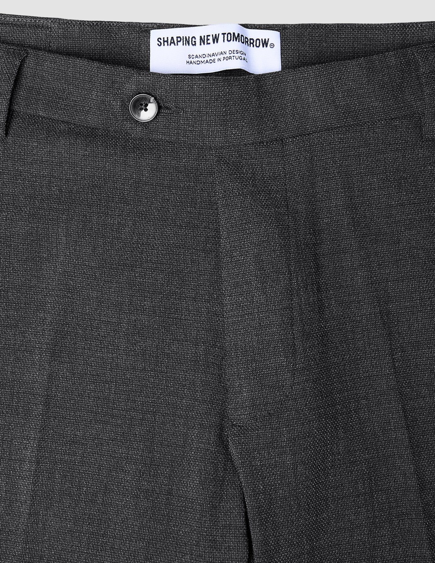 Nahaufnahme der atmungsaktiven, dunkelgrauen Motion Suit-Hose Regular Pepper Grey mit Knopfverschluss und Markenetikett am Bund.