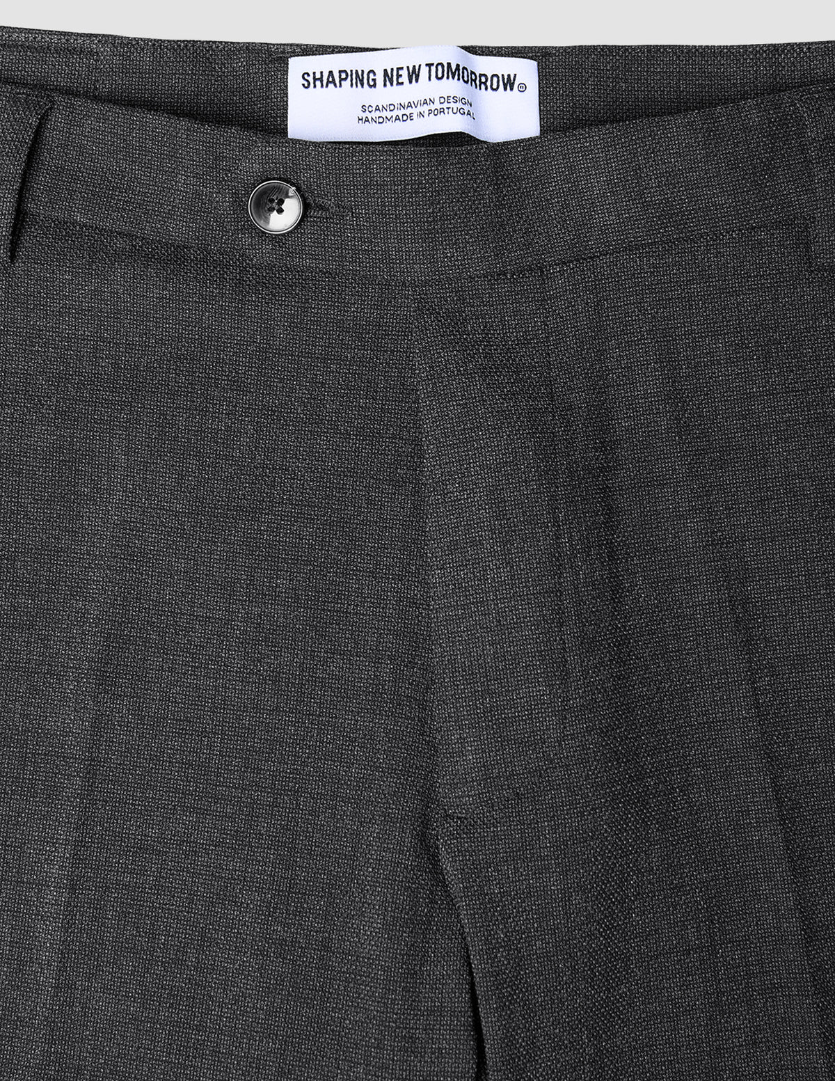 Nahaufnahme der atmungsaktiven, dunkelgrauen Motion Suit-Hose Regular Pepper Grey mit Knopfverschluss und Markenetikett am Bund.