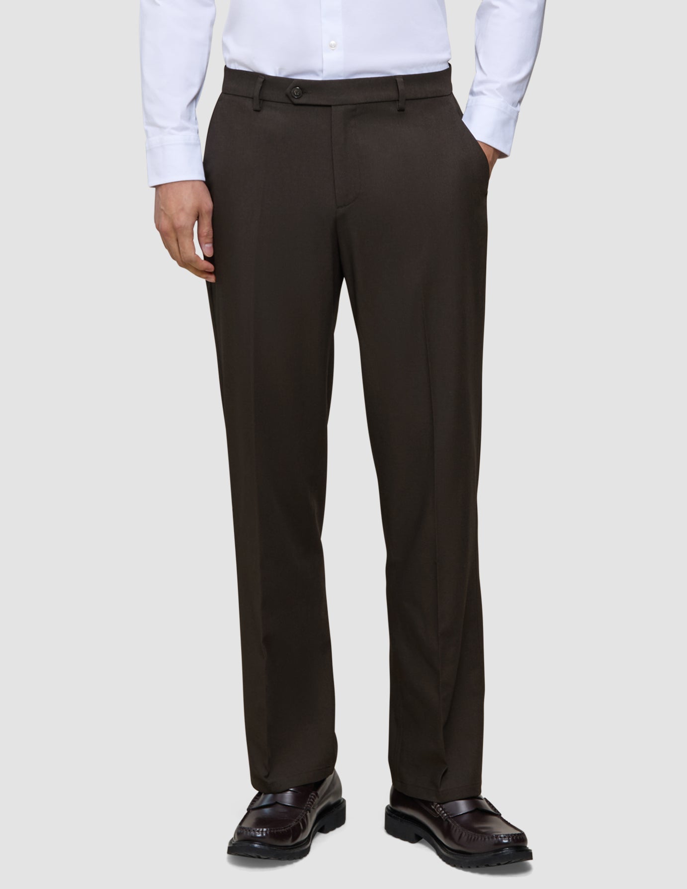 Eine Person, die ein weißes Hemd, eine Motion Suit-Hose in der Passform Relaxed in der Farbe Cognac und dunkelbraune Slipper trägt.
