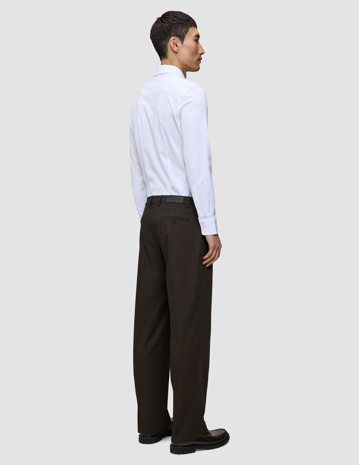 Eine Person in einem weißen Hemd und einer Motion Suit-Hose Relaxed Cognac, im Profil stehend.
