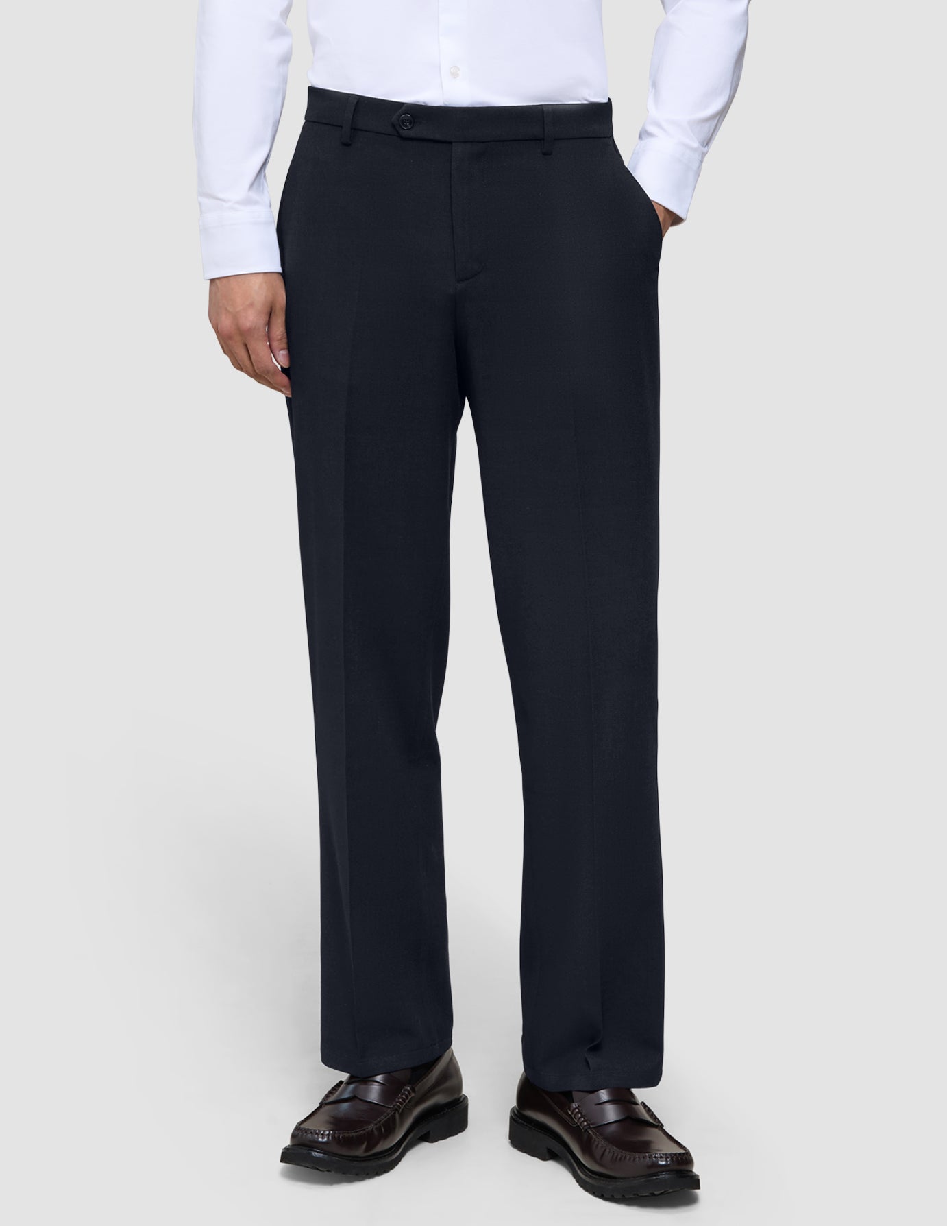 Eine Person, die eine Motion Suit-Hose Relaxed in Mitternachtsblau, ein weißes Hemd mit Knöpfen und dunkelbraune Slipper trägt.