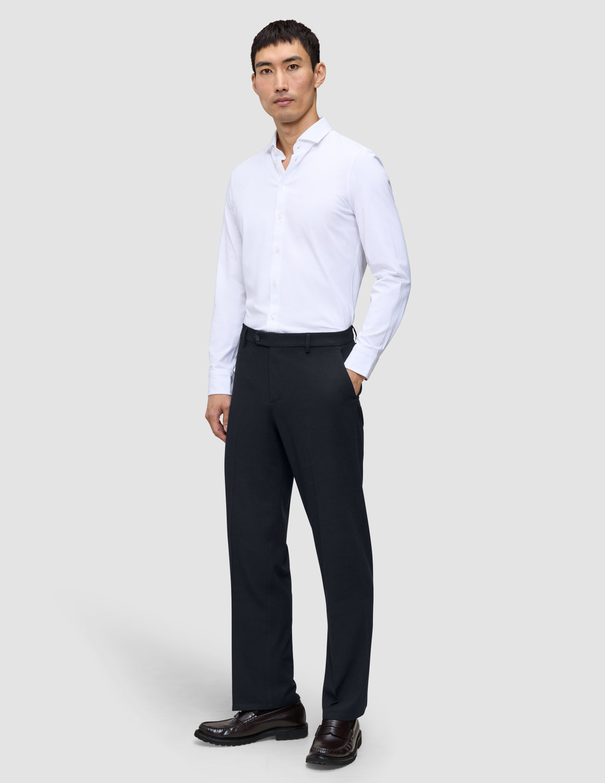 Ein Mann, der ein weißes Hemd und eine Motion Suit-Hose im Relaxed-Schnitt in Mitternachtsblau trägt.
