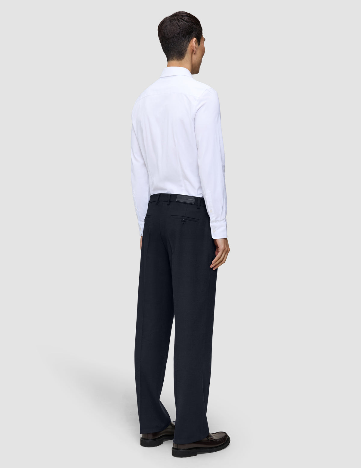 Ein Mann, von hinten gesehen, der ein weißes Hemd und eine Motion Suit-Hose im Relaxed-Schnitt in Mitternachtsblau trägt.