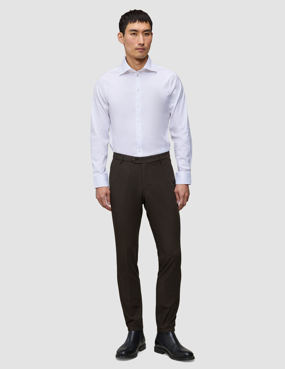 Ein Mann trägt ein weißes Hemd, eine Motion Suit-Hose in der Passform Slim in der Farbe Cognac sowie schwarze Lederstiefel und sorgt so für einen eleganten Look.