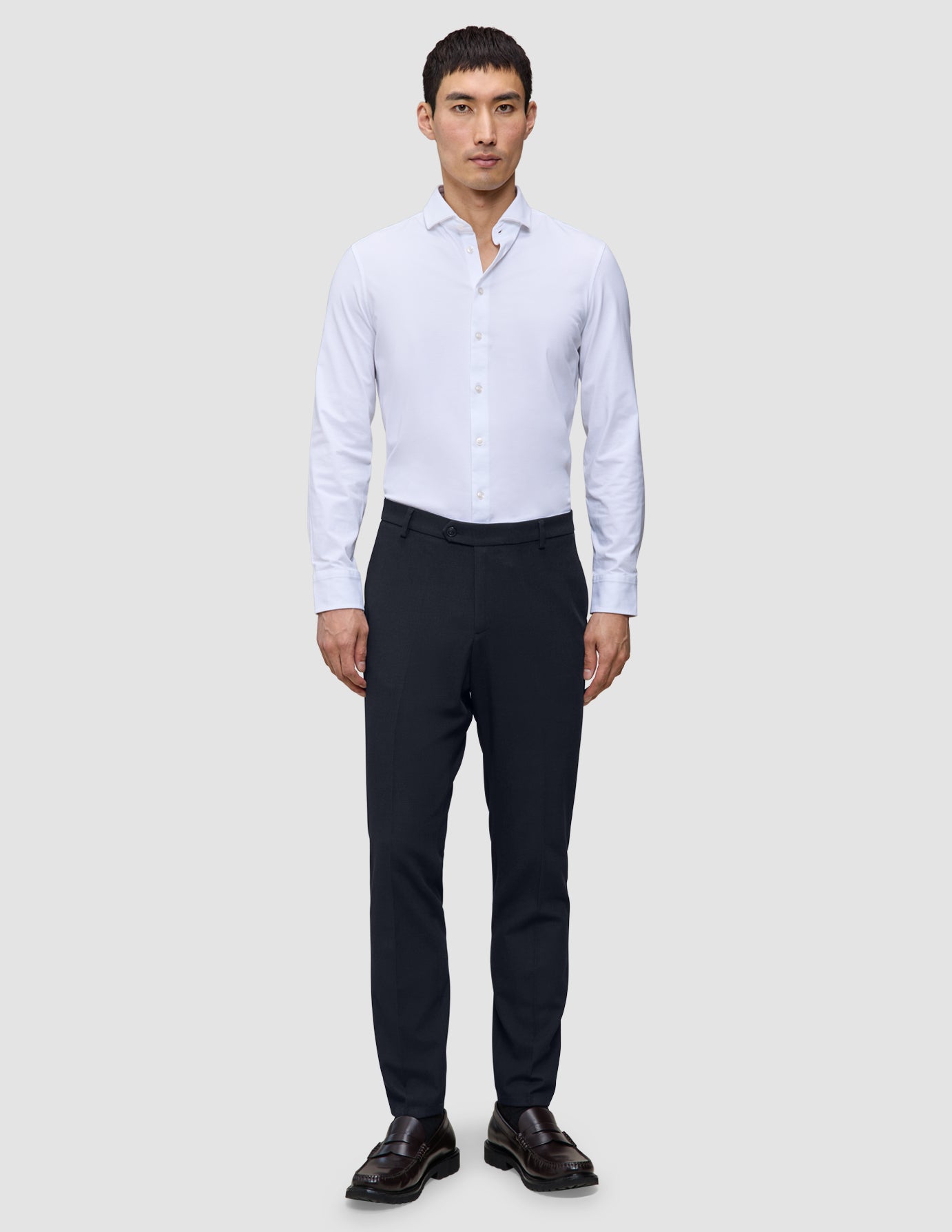 Ein Mann, der ein weißes Hemd und eine dunkelblaue, schmal geschnittene Motion Suit Pants Slim Midnight Blue trägt.