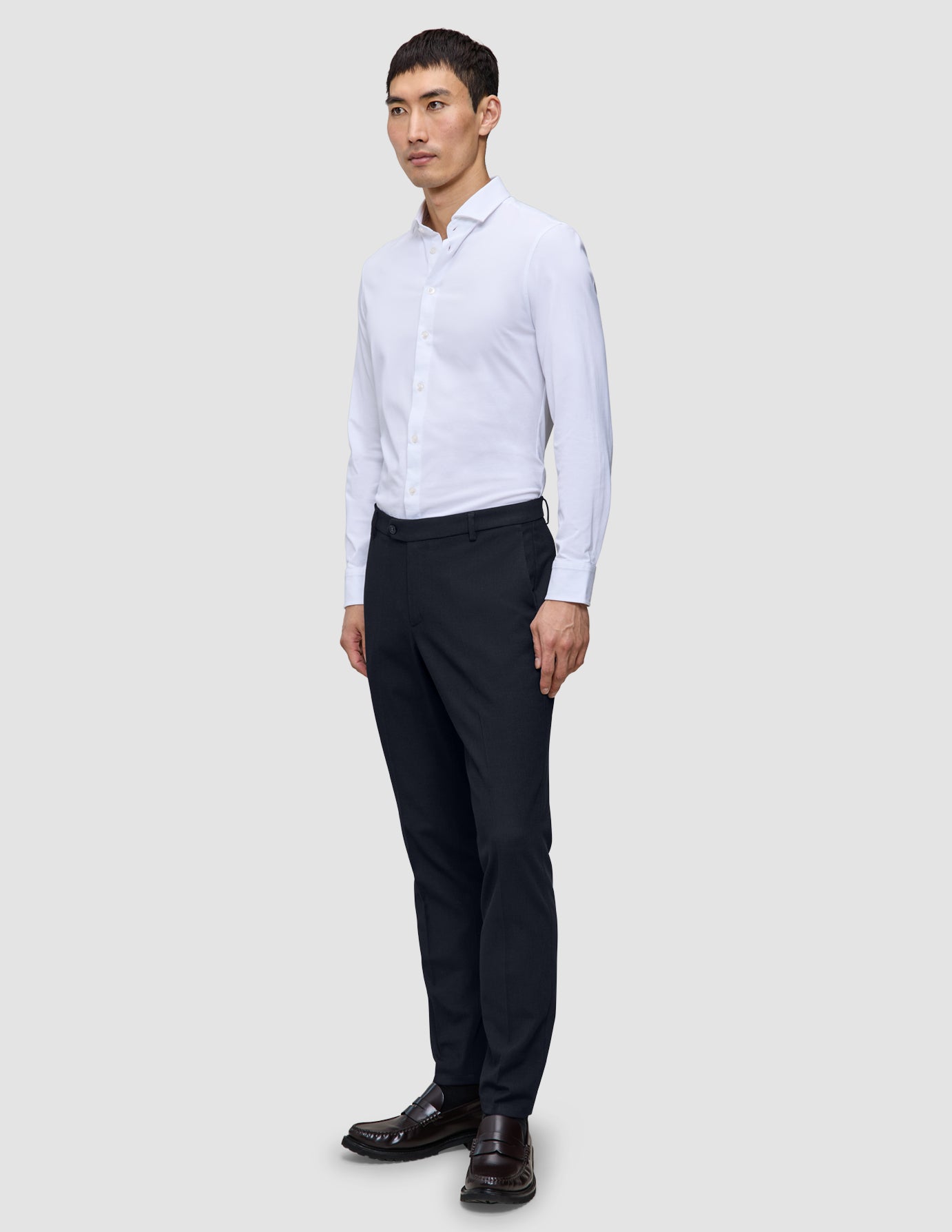 Ein Mann, der ein weißes, langärmeliges Hemd mit Knöpfen und eine Motion Suit Pants Slim in Mitternachtsblau trägt.