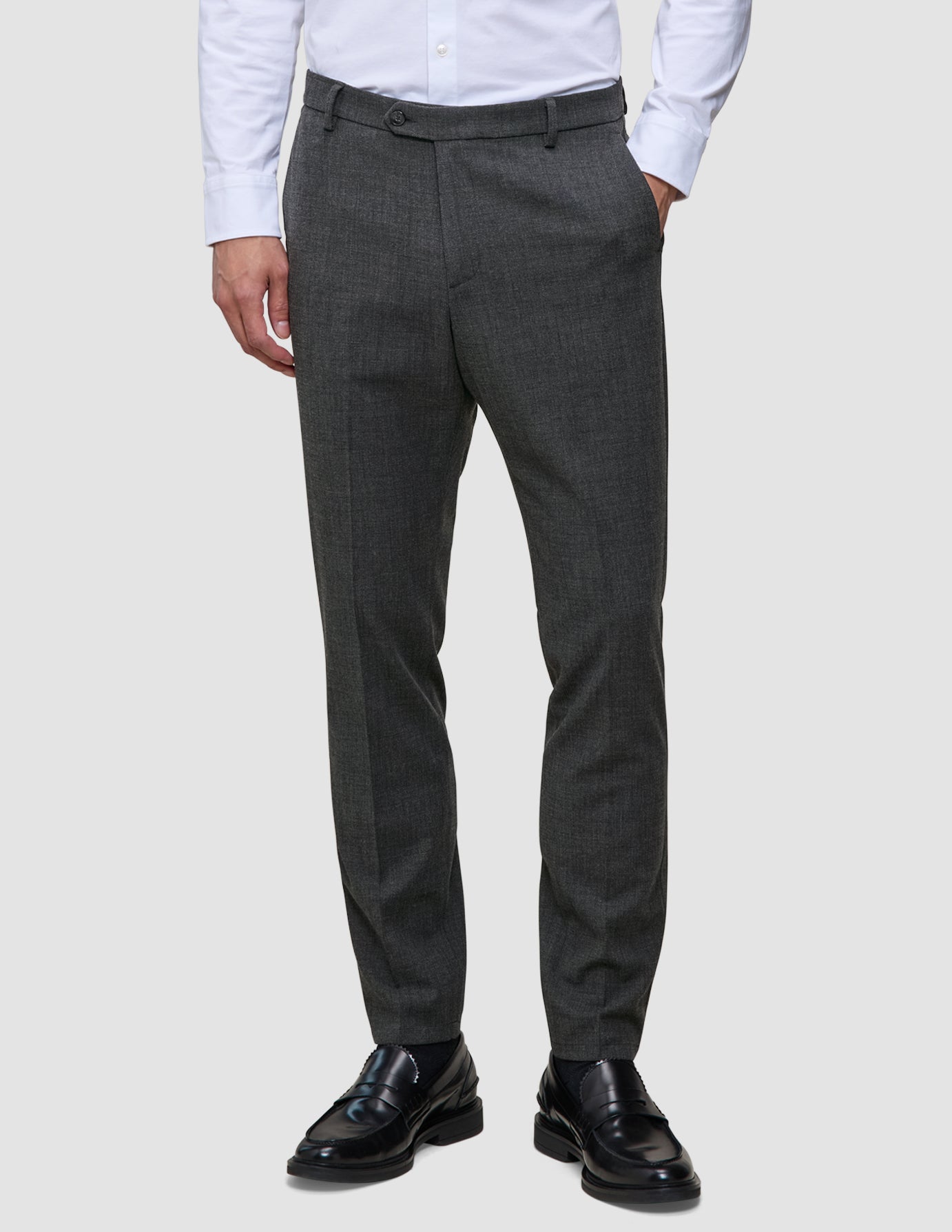 Eine Person, die ein weißes Hemd, eine Motion Suit-Hose in der Farbe Slim Pepper Grey und schwarze Leder-Loafer trägt.