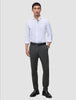 Ein Mann, der ein weißes Hemd, einen schwarzen Gürtel, eine Motion Suit-Hose in der Farbe Slim Pepper Grey und schwarze Slipper trägt.