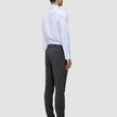 Ein Mann, von hinten gesehen, der ein weißes Hemd, eine Motion Suit-Hose in der Farbe Slim Pepper Grey und schwarze Slipper trägt.