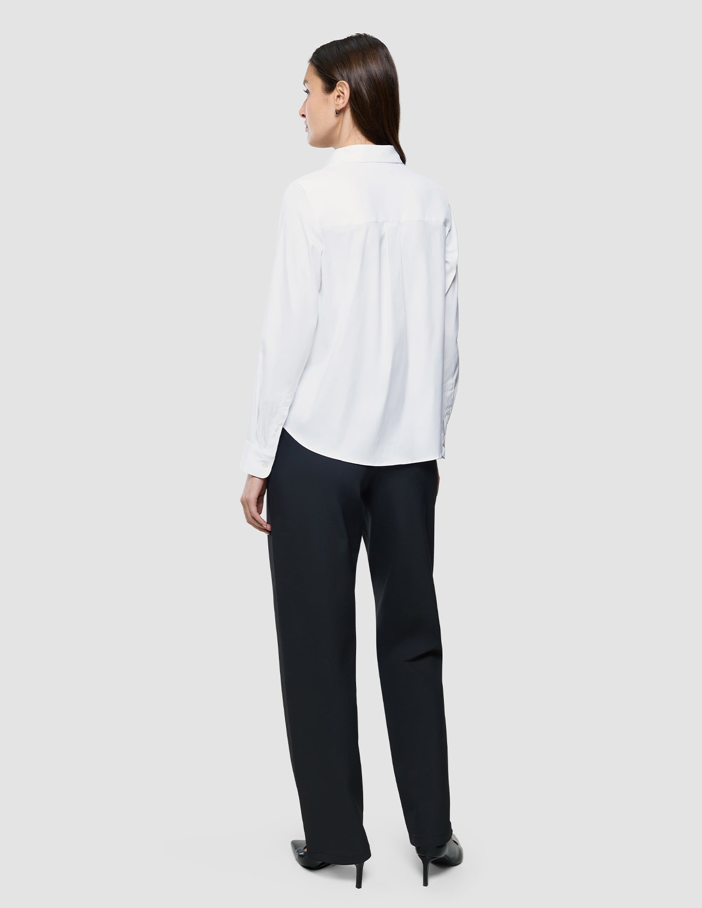 Eine Frau, von hinten gesehen, die ein weißes „Women Oxford Shirt White Regular“ und eine schwarze Hose trägt.