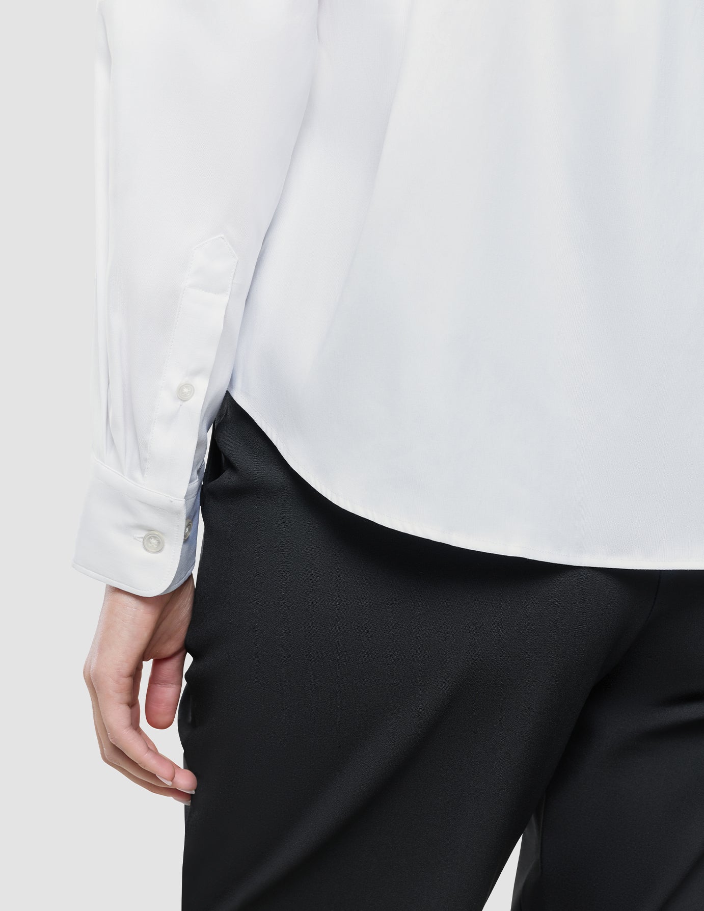 Eine Person, die ein weißes Damen-Oxford-Hemd in regulärer Passform trägt, das in eine schwarze Hose gesteckt ist.