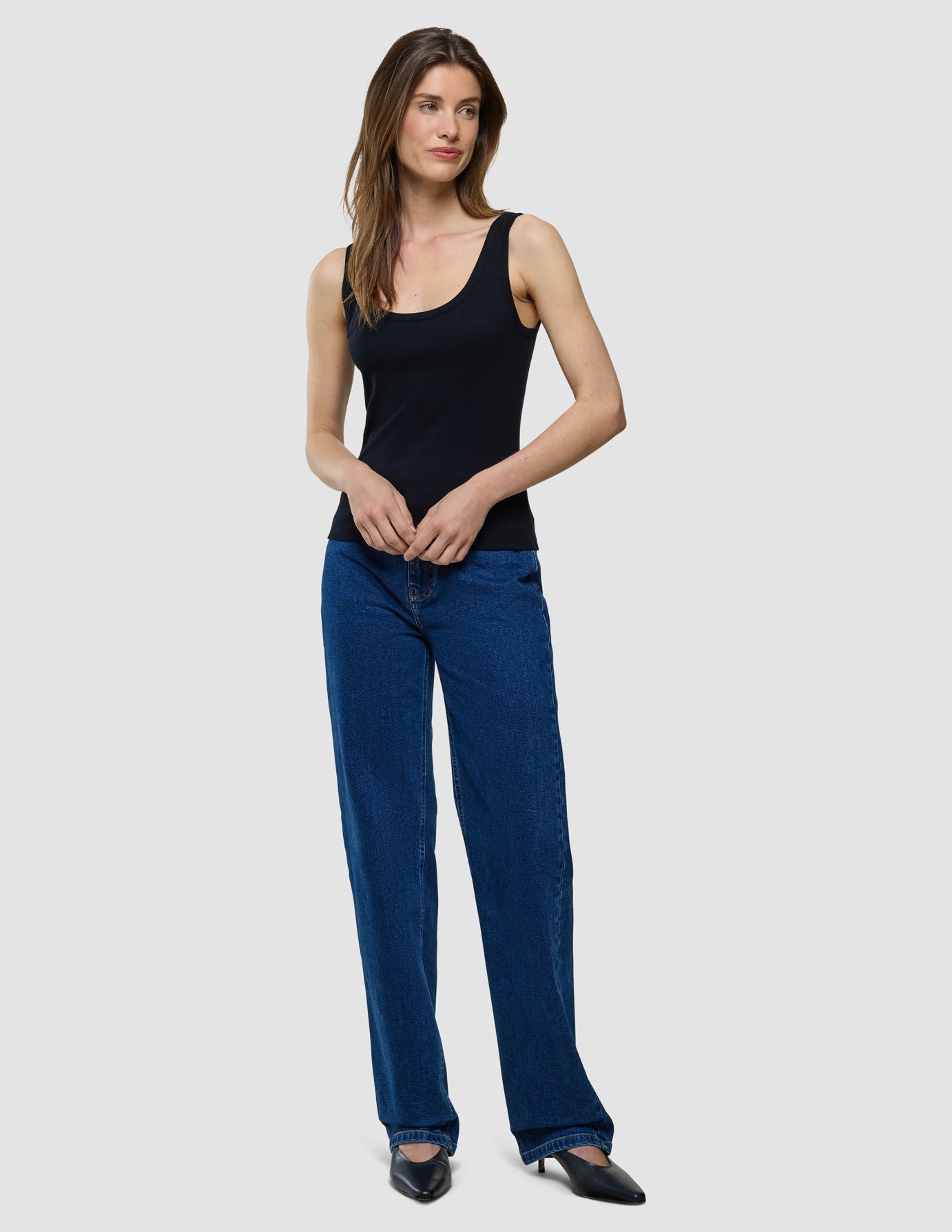 Eine Frau, die ein schwarzes Ripp-Tanktop und eine blaue Jeans trägt.