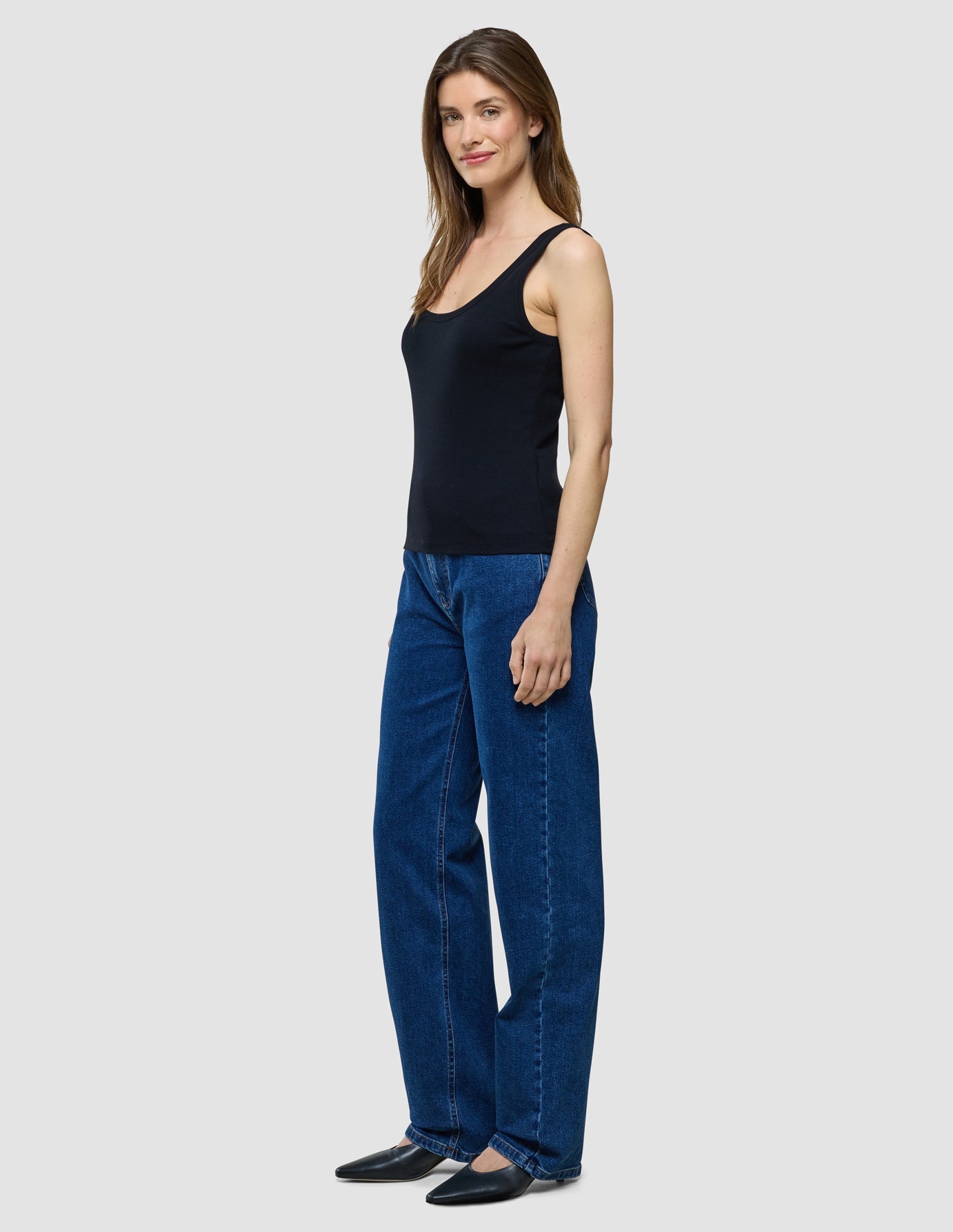 Eine Frau im Profil, die ein schwarzes Rib-Tanktop und eine blaue Jeans trägt.