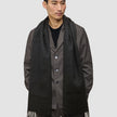 Ein Mann trägt eine dunkelbraune Jacke über einem schwarzen Hemd und einen Scarf Black, einen langen, mit Fransen verzierten Schal aus Kaschmirwolle im minimalistischen skandinavischen Design.
