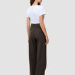 Eine Frau, von hinten gesehen, trägt ein weißes T-Shirt und eine braune Serene Pants Wide Walnut Herringbone mit weitem Bein und dezentem vertikalem Nadelstreifenmuster, die das minimalistische skandinavische Design verkörpert.