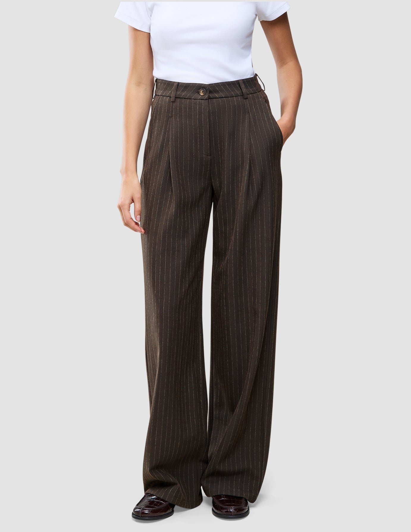 Dunkelbraune Serene-Hose mit hoher Taille im Wide Walnut Herringbone-Muster, mit feinen vertikalen Nadelstreifen und weitem Beinschnitt, kombiniert mit einem weißen T-Shirt.