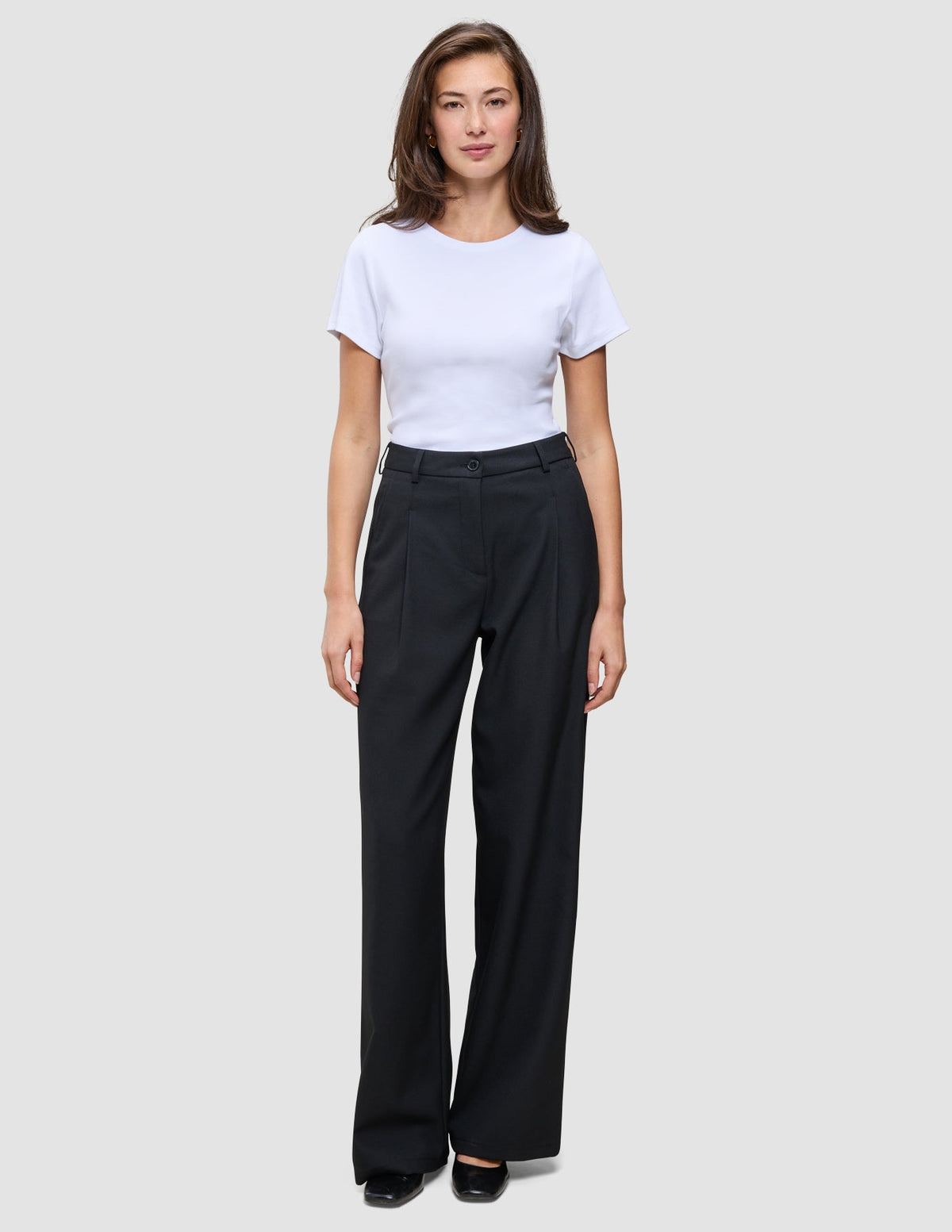 Eine Person, die ein weißes, kurzärmeliges T-Shirt mit Rundhalsausschnitt und die Serene Pants Wide Black trägt – eine Hose mit hoher Taille und weitem Bein im skandinavischen Design.