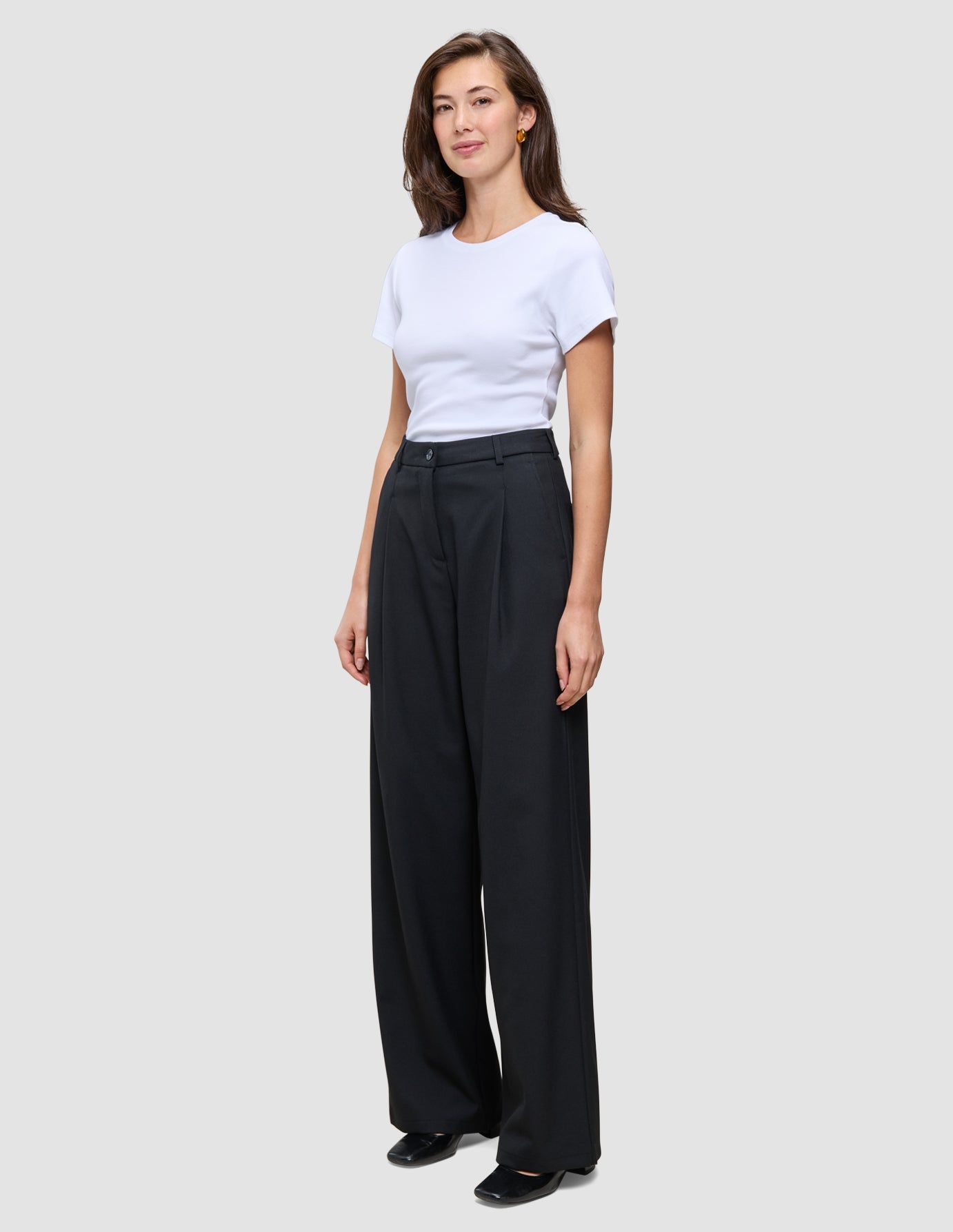 Eine Frau trägt ein weißes T-Shirt und die Serene Pants Wide Black – eine Hose mit weitem Bein und hoher Taille im minimalistischen, skandinavischen Design.
