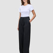 Eine Frau trägt ein weißes T-Shirt, das sie in eine hoch taillierte, weit geschnittene Serene Pants Wide Black gesteckt hat.