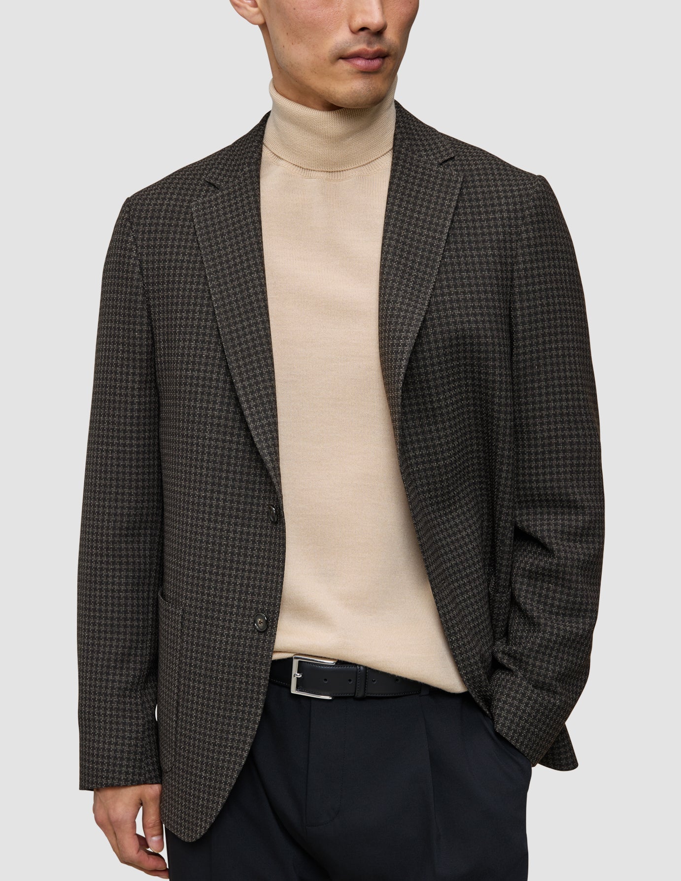 Ein Mann im Strick-und-Blazer-Look: ein Merino-Strickpullover unter einem zeitlosen Wollblazer, eine dunkle Hose und ein schwarzer Gürtel.