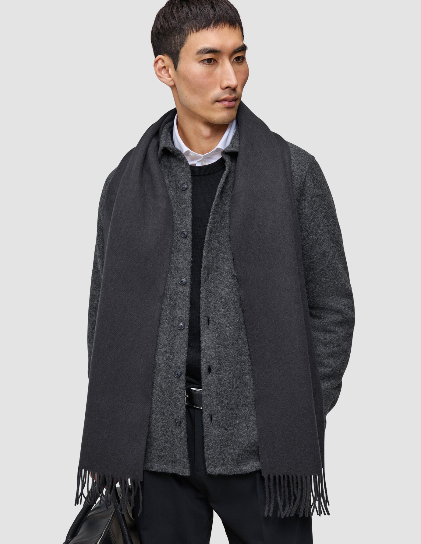 Eine Person, die einen anthrazitfarbenen Schal aus hochwertigem Merinowolle über einem dunklen, doppellagigen Woll-Overshirt und einer schwarzen Hose aus der Kollektion Layers that work trägt.