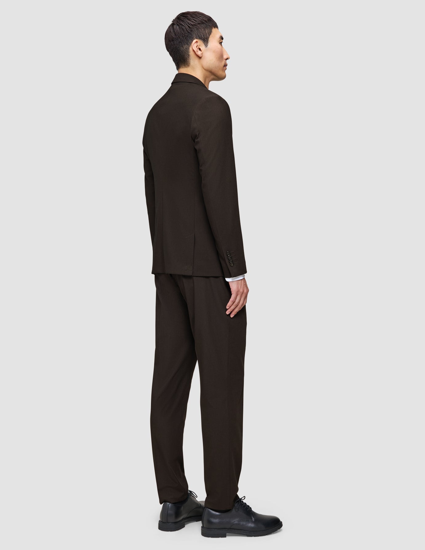 Ein Mann im Profil trägt einen dunkelbraunen Anzug, der einfach zu allem passt, ein elegantes weißes Hemd und schwarze Lederschuhe.
