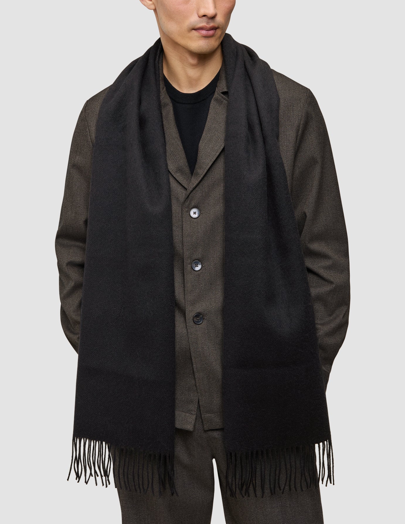 Eine Person, die ein dunkelbraunes Atelier Overshirt und eine dazu passende Atelier Pants als eine etwas andere Art von Anzug über einem schwarzen Hemd trägt, mit einem langen schwarzen Schal um den Hals drapiert.