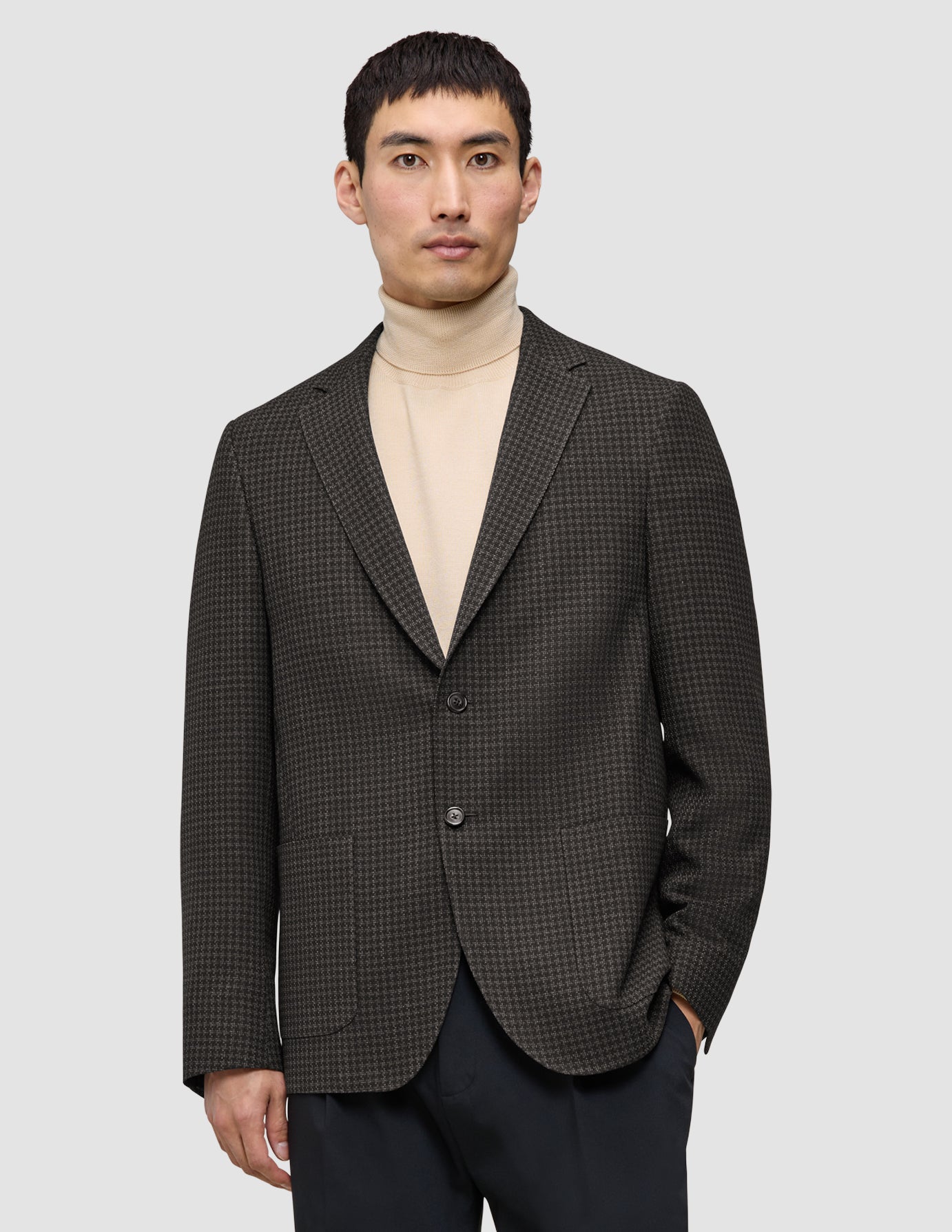 Ein Mann, der einen dunkelbraunen, karierten Timeless Wool Blazer Slim über einem beigen Rollkragenpullover trägt.