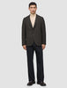 Ein Mann trägt einen dunkelbraunen, karierten Timeless Wool Blazer Slim über einem beigen Pullover mit Stehkragen und einer dunklen Hose.