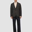 Ein Mann trägt einen dunkelbraunen, karierten Timeless Wool Blazer Slim über einem beigen Pullover mit Stehkragen und einer dunklen Hose.