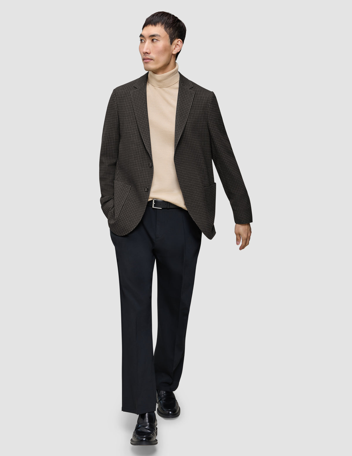Ein Mann, der einen dunkelbraunen, karierten Timeless Wool Blazer Slim über einem hellbraunen Rollkragenpullover, einer dunklen Hose und schwarzen Loafern trägt.