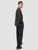 Ein Mann, der einen dunkelbraunen, karierten Timeless Wool Blazer Slim über einem beigen Rollkragenpullover und einer dunklen Hose trägt, blickt über seine Schulter.