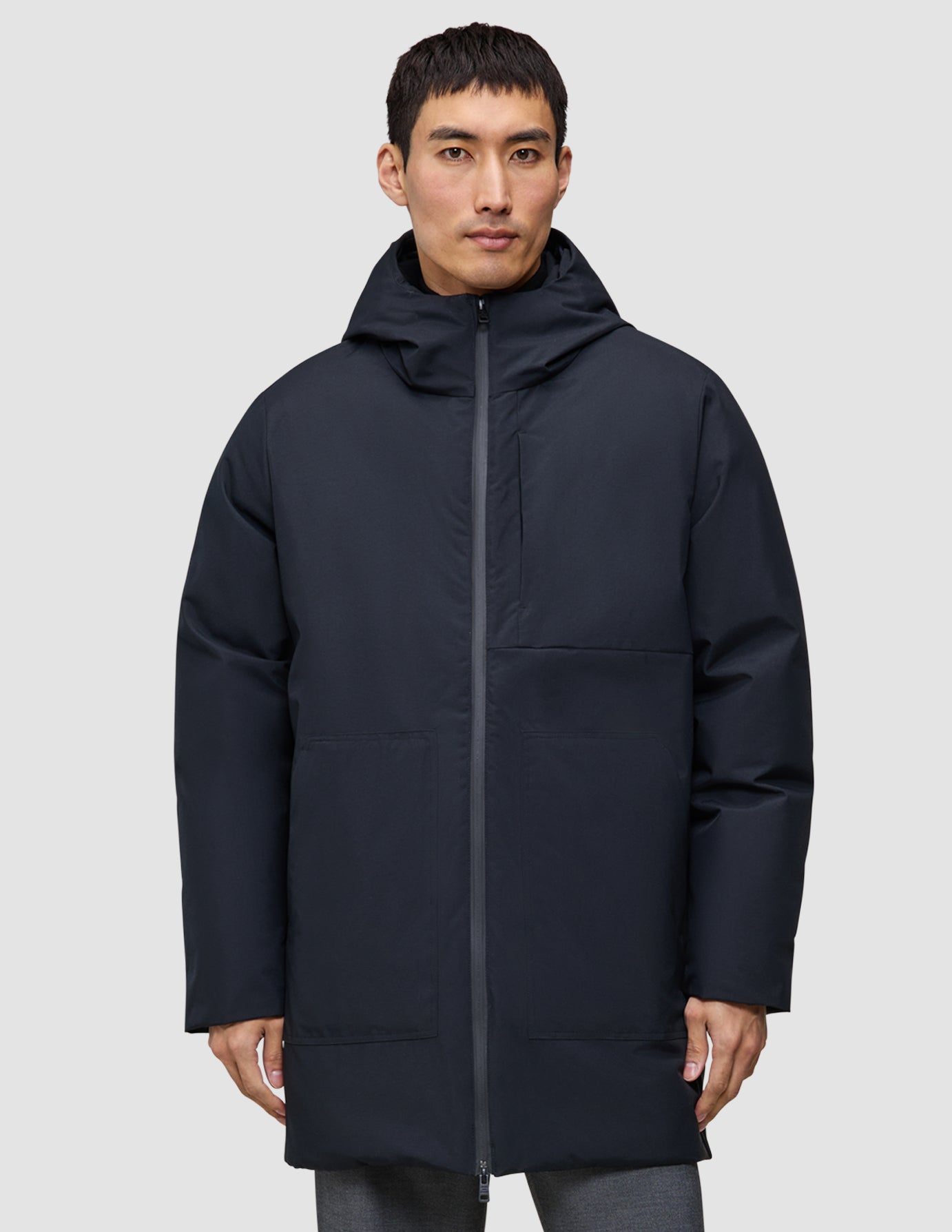 Ein Mann trägt eine schwarze Utility-Jacke mit Kapuze und Reißverschluss aus recyceltem Polyester.
