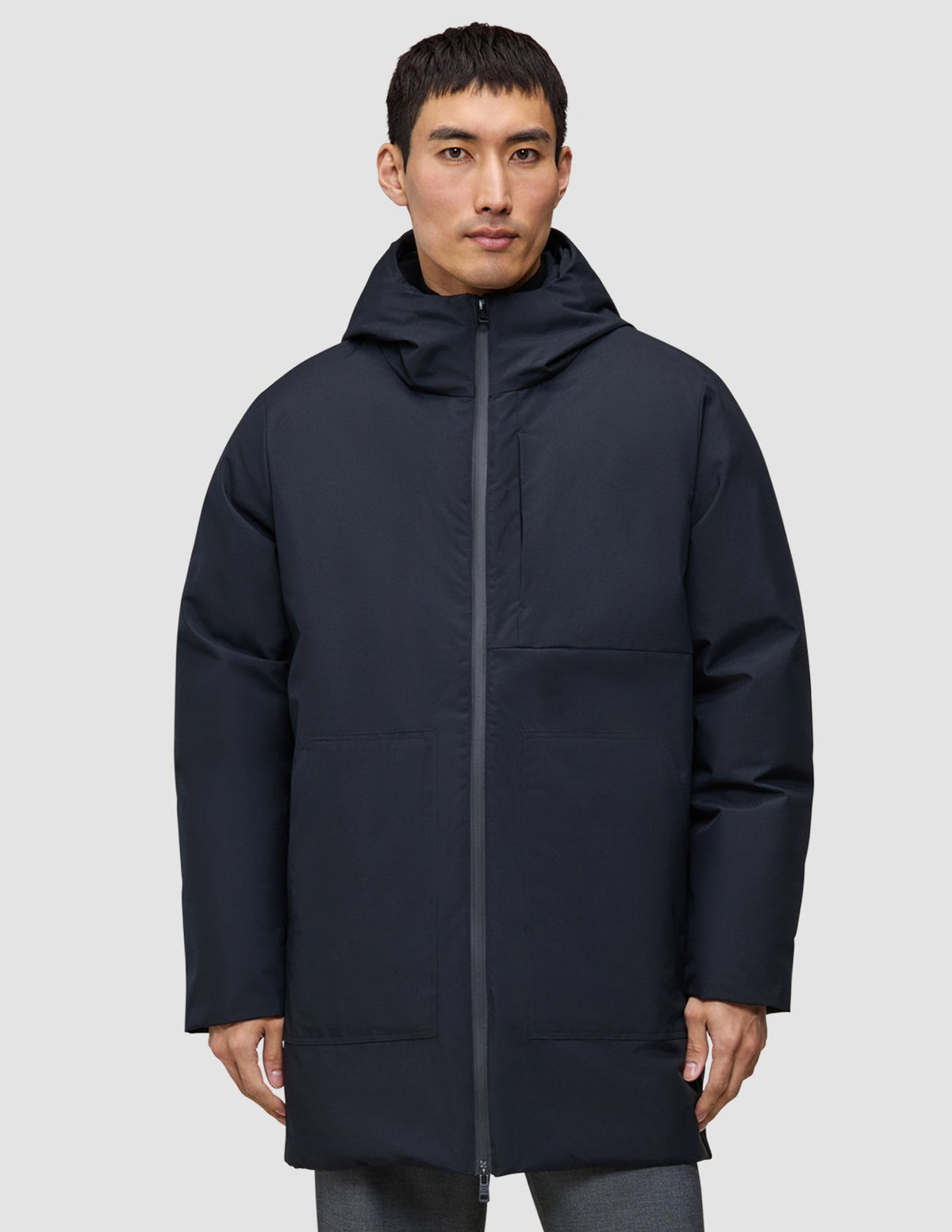 Ein Mann trägt eine schwarze Utility-Jacke mit Kapuze und Reißverschluss aus recyceltem Polyester.