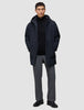 Ein Mann, der eine schwarze Utility-Jacke aus recyceltem Polyester über einem schwarzen Pullover mit Reißverschluss am Kragen und einer grauen Hose trägt.