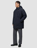 Eine Person, die eine schwarze Utility-Jacke mit Kapuze aus recyceltem Polyester und eine graue Hose trägt.