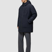 Eine Person, die eine schwarze Utility-Jacke mit Kapuze aus recyceltem Polyester und eine graue Hose trägt.