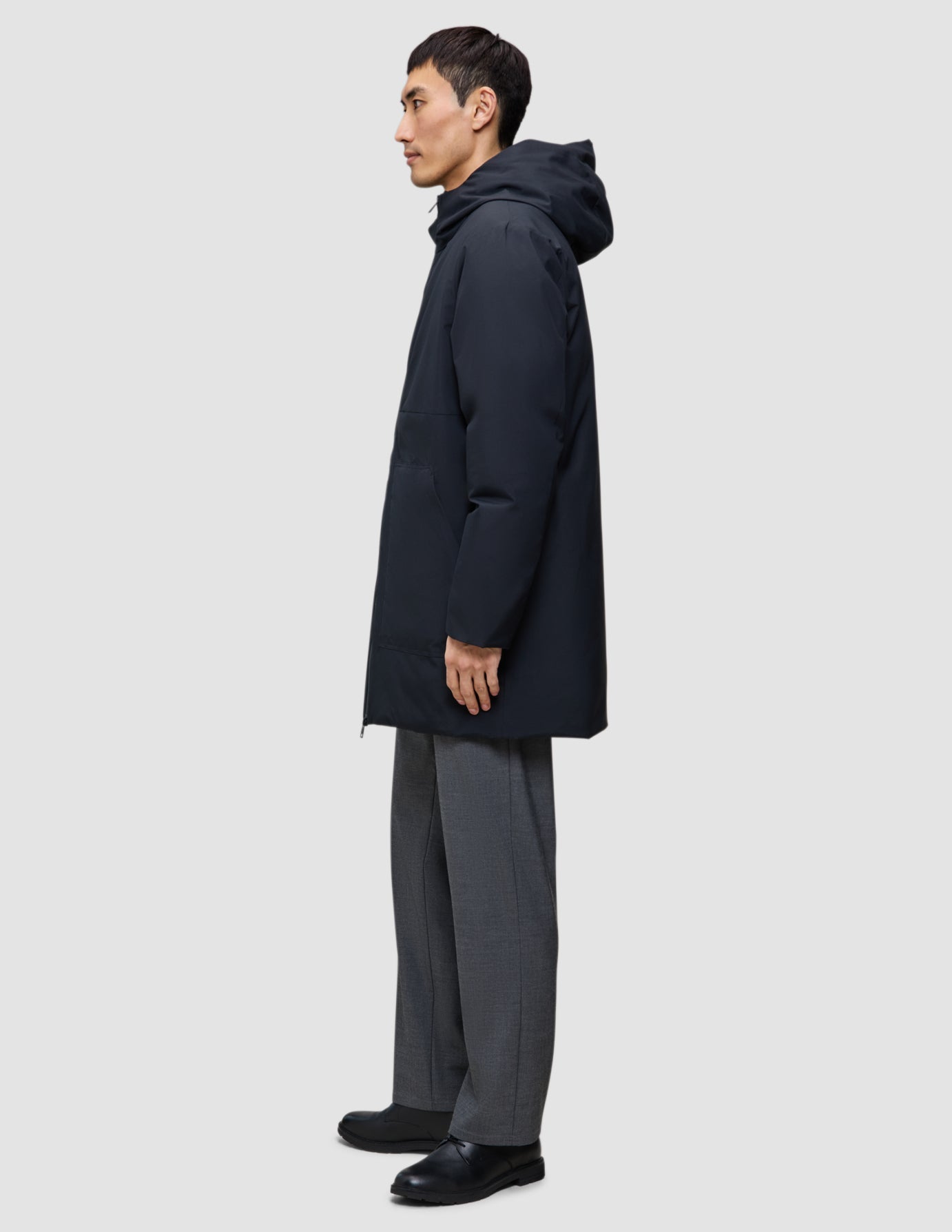 Seitenansicht einer Person, die eine schwarze Utility-Jacke trägt: schwarze Jacke aus recyceltem Polyester, graue Hose und schwarze Schuhe.