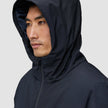 Eine Person, die von der Seite gezeigt wird und eine schwarze Utility-Jacke trägt, wobei die Kapuze hochgezogen ist.