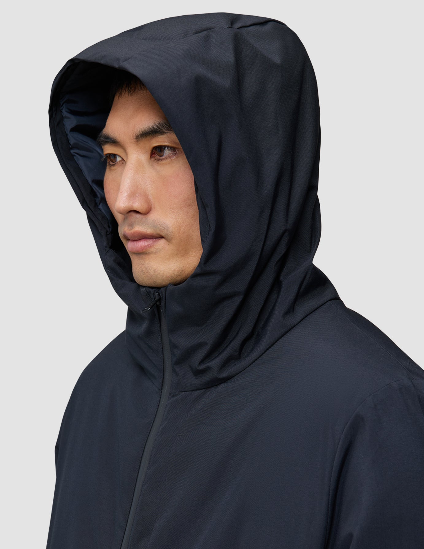 Eine Person, die von der Seite gezeigt wird und eine schwarze Utility-Jacke trägt, wobei die Kapuze hochgezogen ist.
