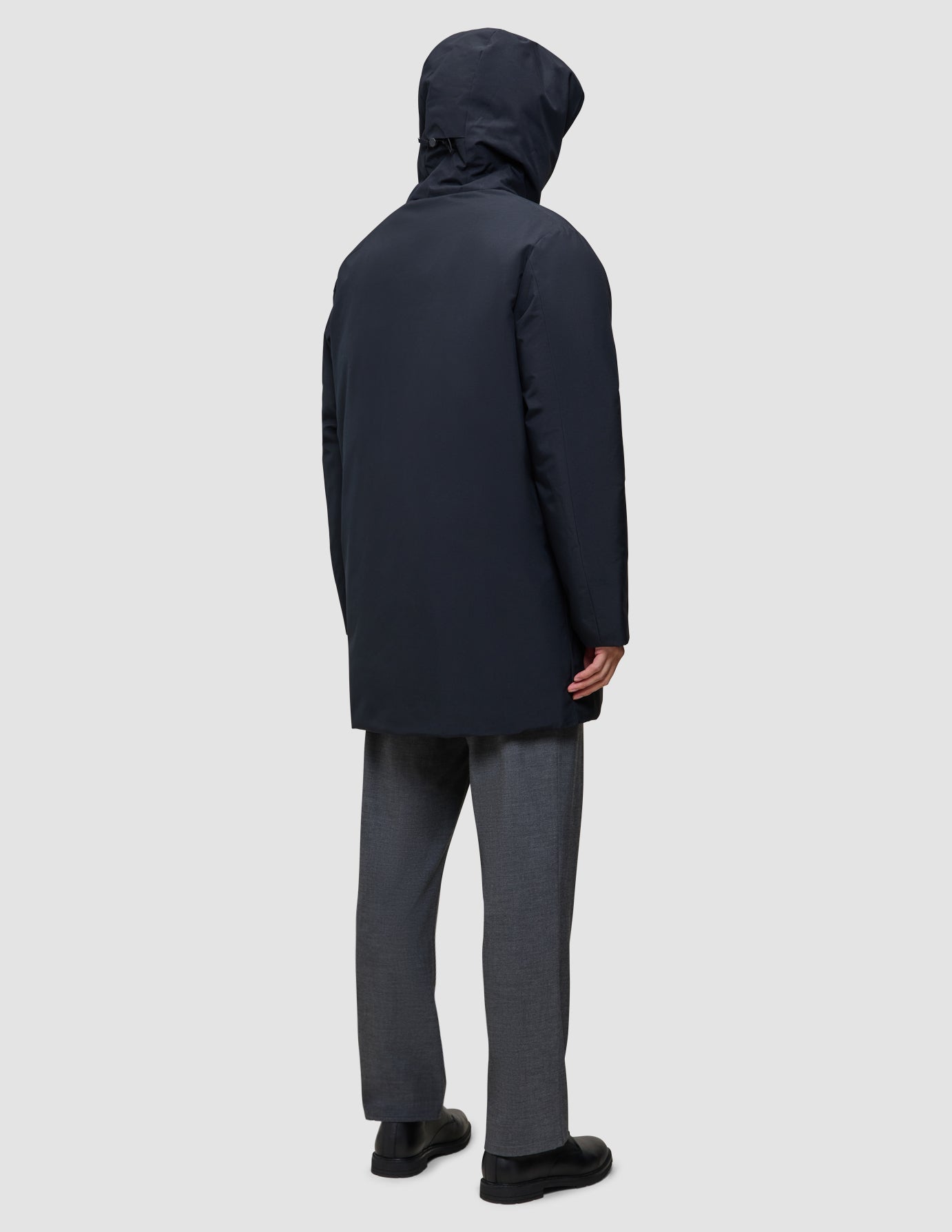 Rückansicht einer Person, die eine schwarze Utility-Jacke aus recyceltem Polyester trägt, kombiniert mit einer grauen Hose und schwarzen Schuhen.